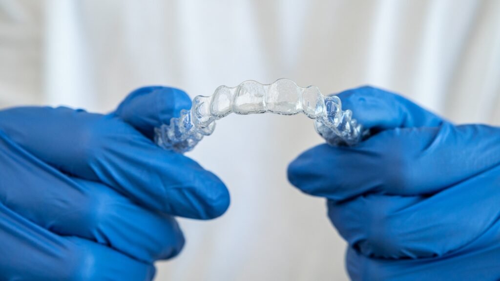 Hand in gloves holding dental aligner retainer. Invisible orthodontic retainer